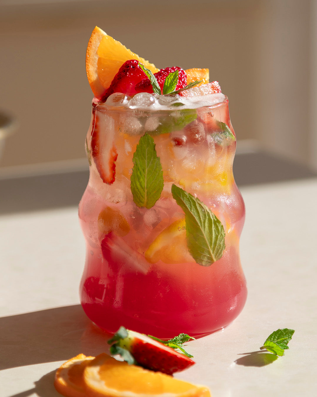 Fruity cocktail with ice and garnishes on a light surface