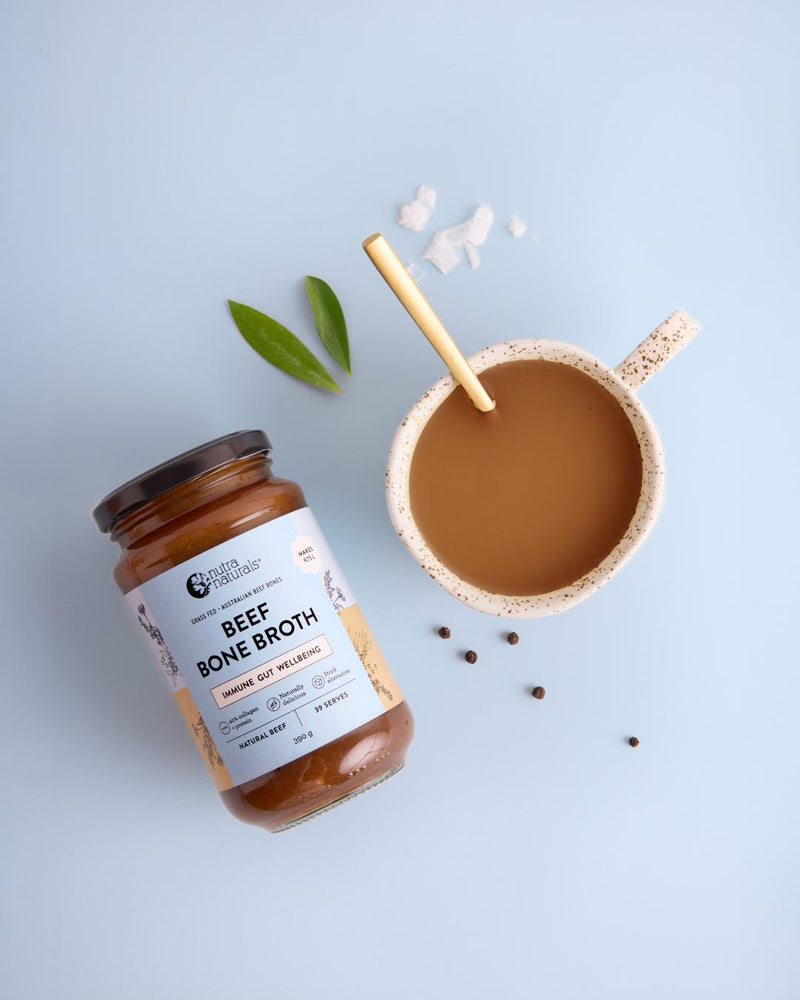 Beef Bone Broth canister next to a ceramic mug filled with the prepared broth and a wooden spoon