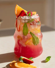 Fruity cocktail with ice and garnishes on a light surface