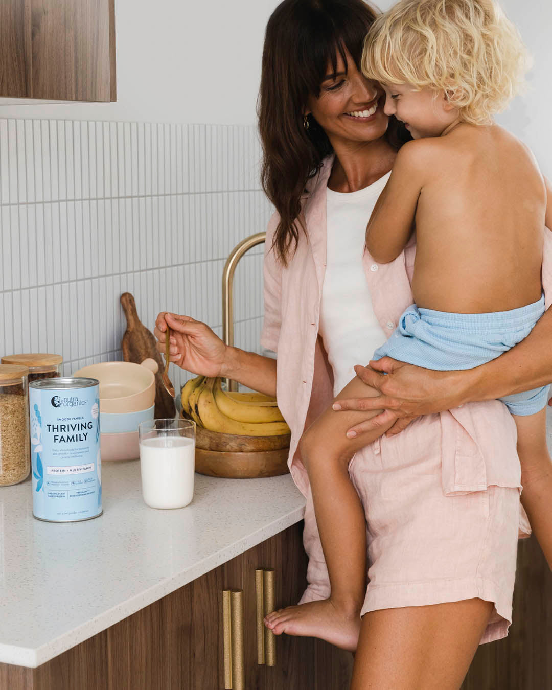 Mom holding her child and showing Thriving Family Smooth canister and glass on the counter